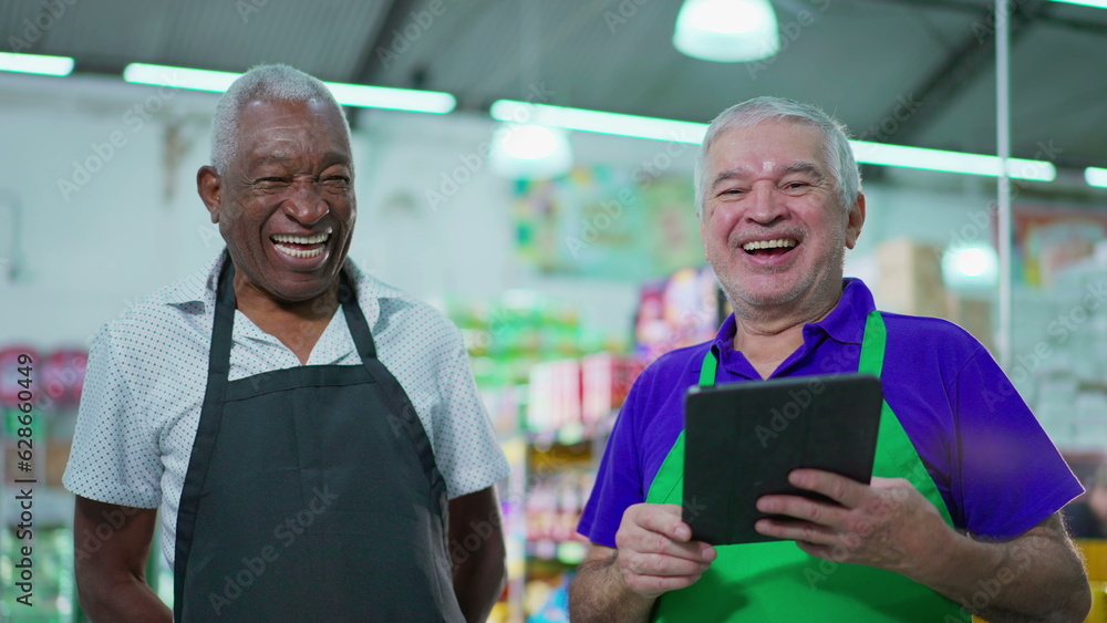 Joyful diverse Brazilian senior staff workers of supermarket chain smiling at camera with table and uniforms. African American older employee and a caucasian person laughing together Joyful diverse Brazilian senior staff workers of supermarket chain smiling at camera with table and uniforms. African American older employee and a caucasian person laughing together