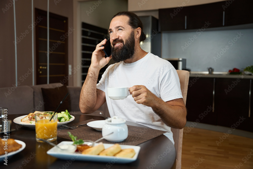Bearded man is talking on the phone at breakfast Bearded man is talking on the phone at breakfast