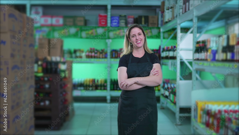 Happy Female Grocery Store Employee standing in supermarket aisle with arms crossed smiling next to products Happy Female Grocery Store Employee standing in supermarket aisle with arms crossed smiling next to products