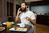 Bearded man is talking on the phone at breakfast