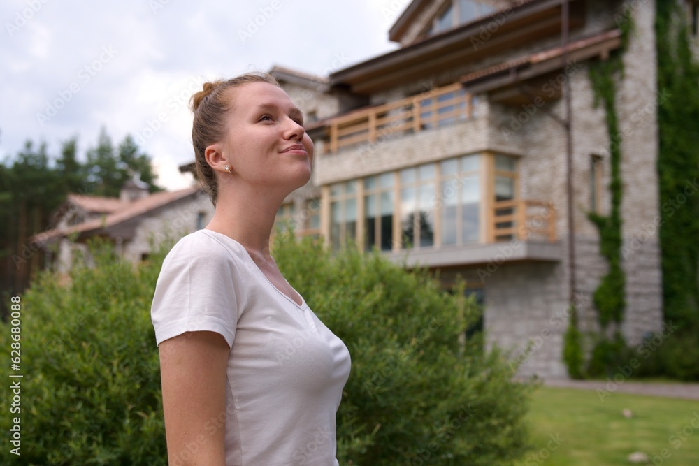 Portrait of happy young woman standing in the garden outside her luxury home and smiling and relax outside Portrait of happy young woman standing in the garden outside her luxury home and smiling and relax outside