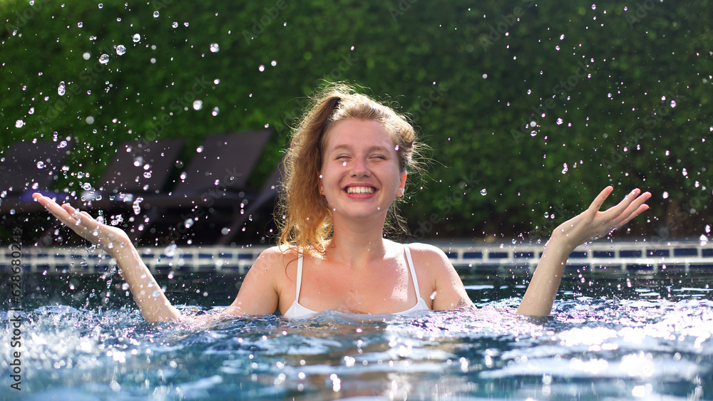 Portrait of happy cheerful young woman having fun, swim in swimming pool outdoors at summer sunny day, enjoy summer vacation, look at camera 