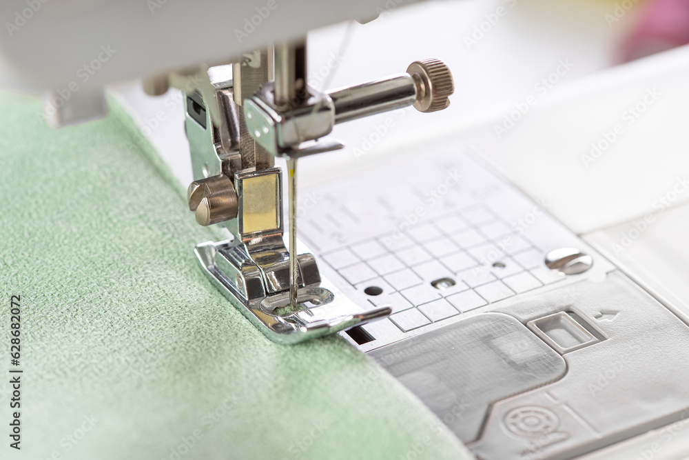 Modern sewing machine presser foot with green fabric and thread, closeup, macro. Sewing process clothes, curtains, upholstery. Business, hobby, handmade, zero waste, recycling, repair concept Modern sewing machine presser foot with green fabric and thread, closeup, macro. Sewing process clothes, curtains, upholstery. Business, hobby, handmade, zero waste, recycling, repair concept