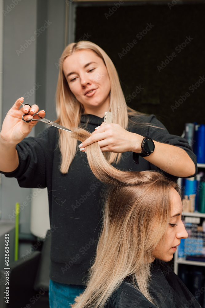 A hairdresser cuts a blonde's hair in a beauty salon. Women's haircut