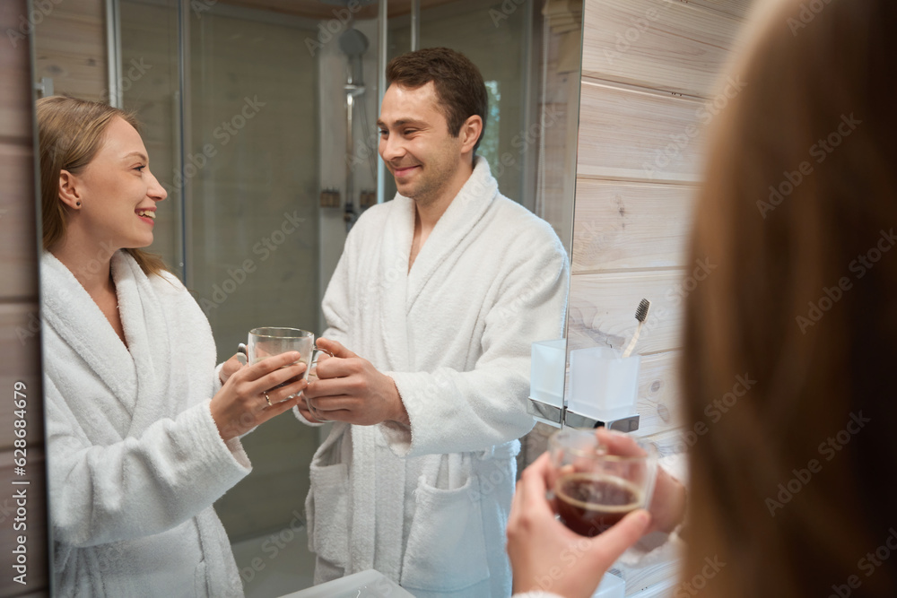 Obraz premium Man giving coffee to woman while standing near bathroom mirror