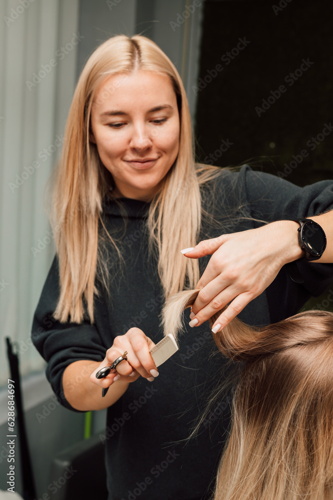 Fototapeta premium A hairdresser cuts a blonde's hair in a beauty salon. Women's haircut