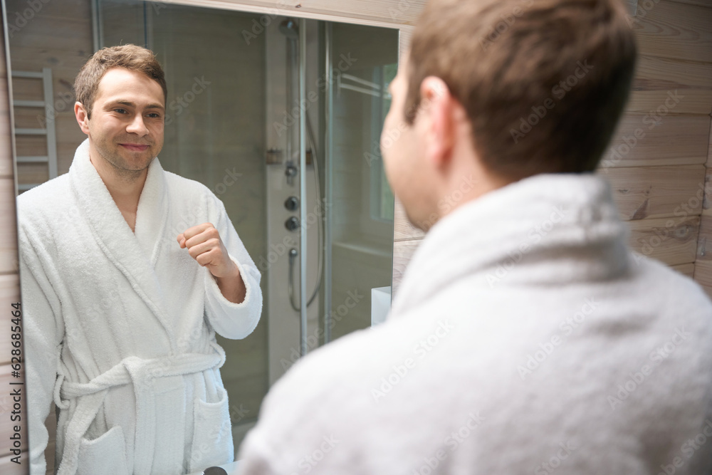 Obraz premium Male in bathrobe looking at himself in bathroom mirror