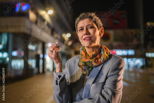One caucasian senior woman stand in the city at night have a cigarette