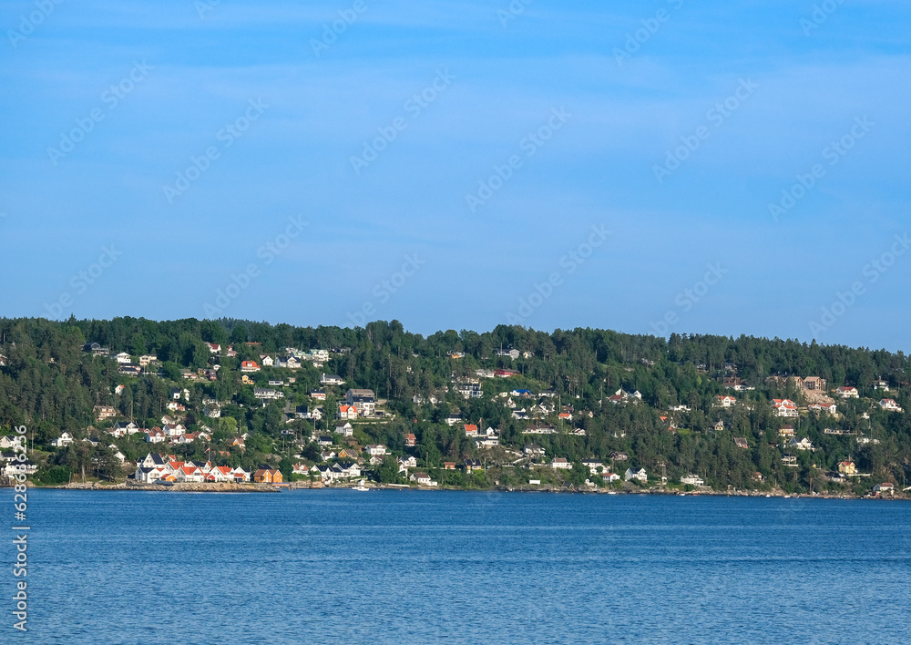 Typische norwegische Häuser an einem Ufer des Oslofjords inmitten grüner Natur, blauner Himmel und sehr viel Copy Space