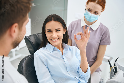 Smiling woman showing ok gesture sign sitting in orthodontic chair photo