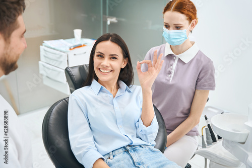 Satisfied with professional teeth treatment woman client showing ok sign