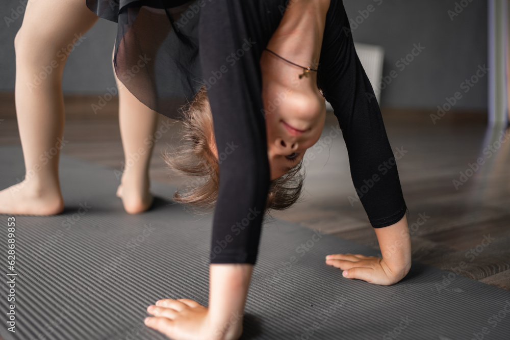 Small girl doing bridge stand exercise in the training studio. Yoga for kids, gymnastics class. Healthy physical development of a child