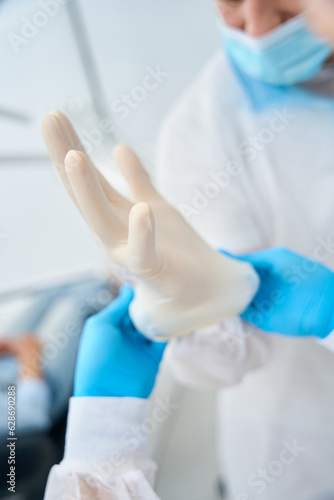 Nurse helping to high-qualified male dental technician to put on sterille gloves