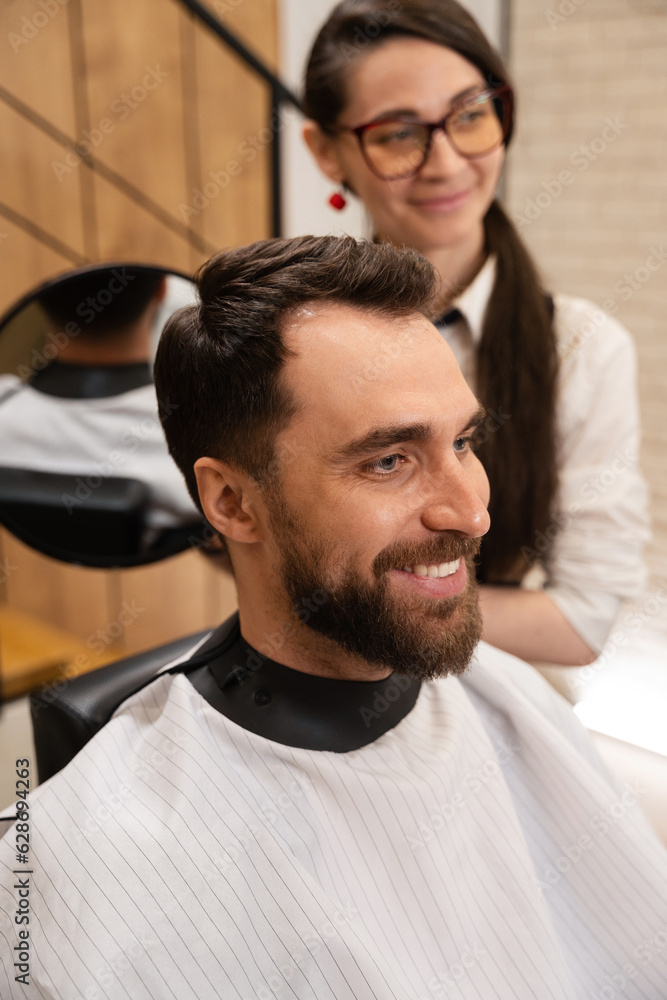 Barber woman demonstrates in the mirror to client his hairstyle Barber woman demonstrates in the mirror to client his hairstyle