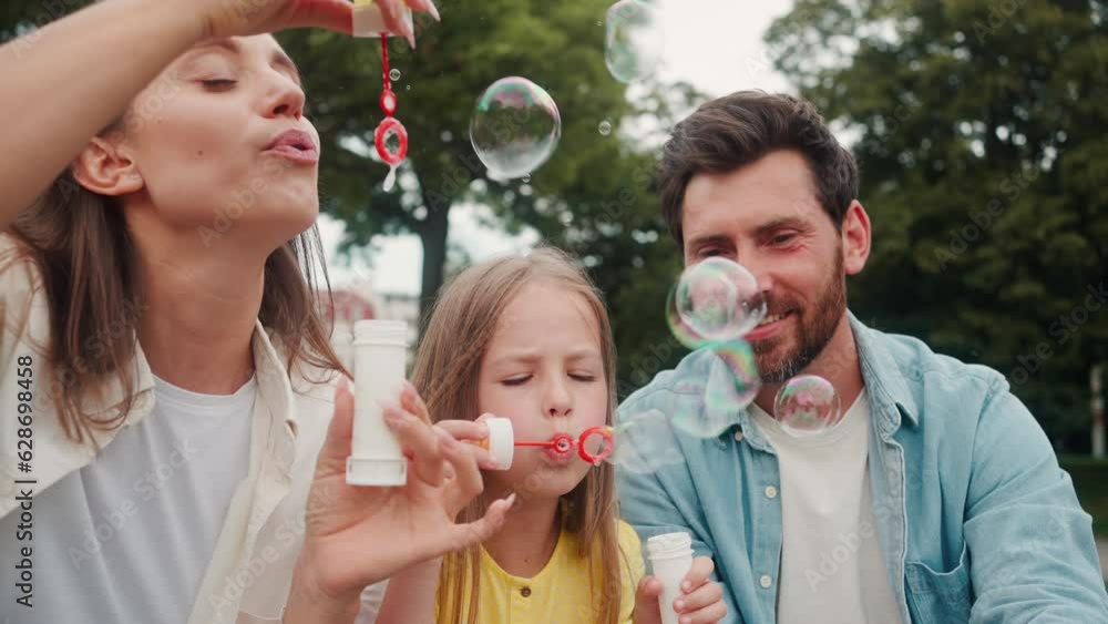 Mother and daughter blow bubbles while father pops in park Mother and daughter blow bubbles while father pops in park