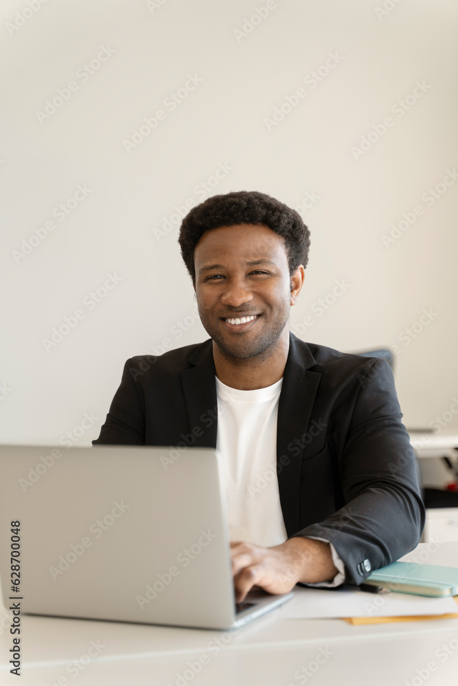 Portrait of beautiful african man using laptop looking at camera on modern office Portrait of beautiful african man using laptop looking at camera on modern office