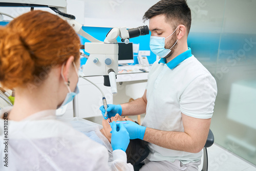 Doctor treats a young female tooth under a microscope