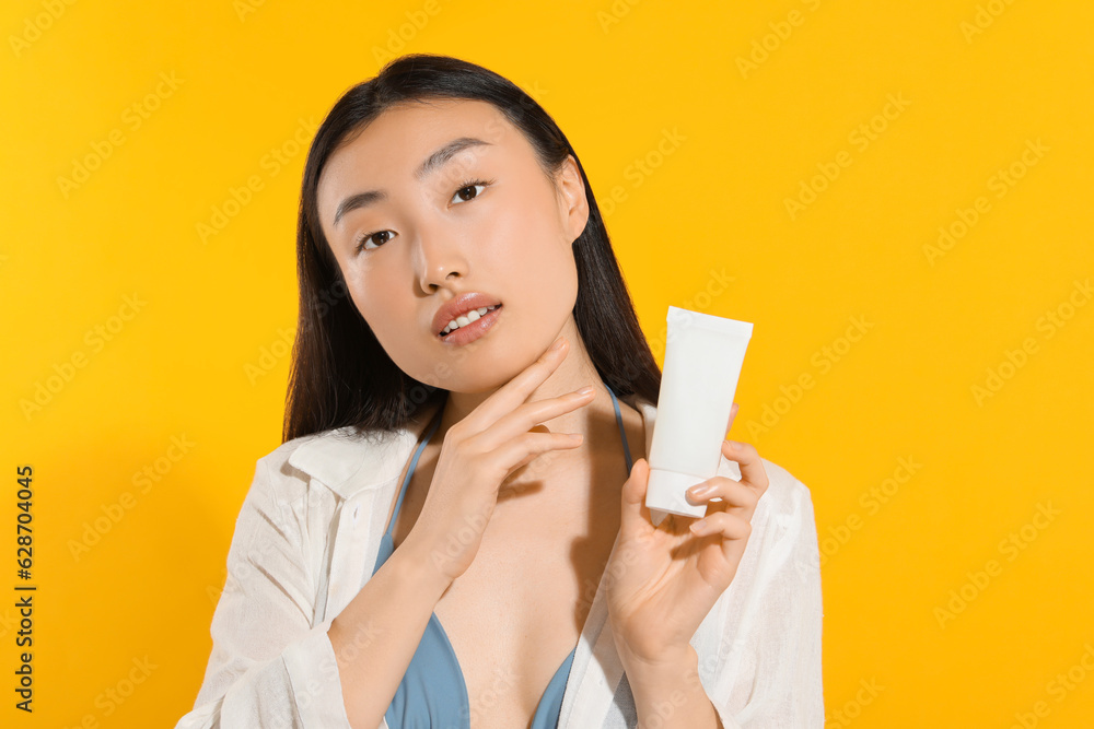 Beautiful young woman holding sun protection cream on orange background Beautiful young woman holding sun protection cream on orange background