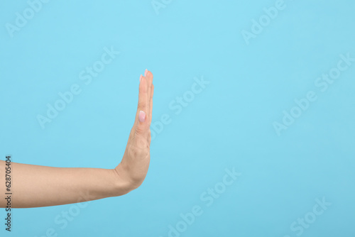 Woman showing stop gesture on light blue background, closeup. Space for text