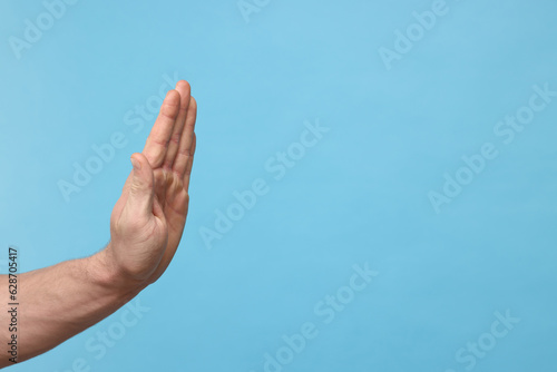 Man showing stop gesture on light blue background, closeup. Space for text