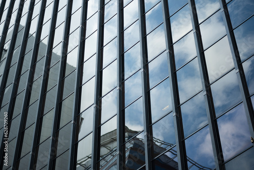 On a high-rise office building, shiny windows reflect back the surrounding architecture and the blue sky.