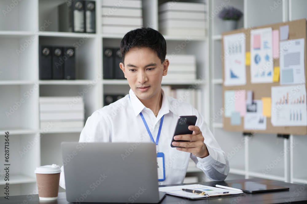 Charming young businessman using smartphone while working on his project with laptop computer. Charming young businessman using smartphone while working on his project with laptop computer.