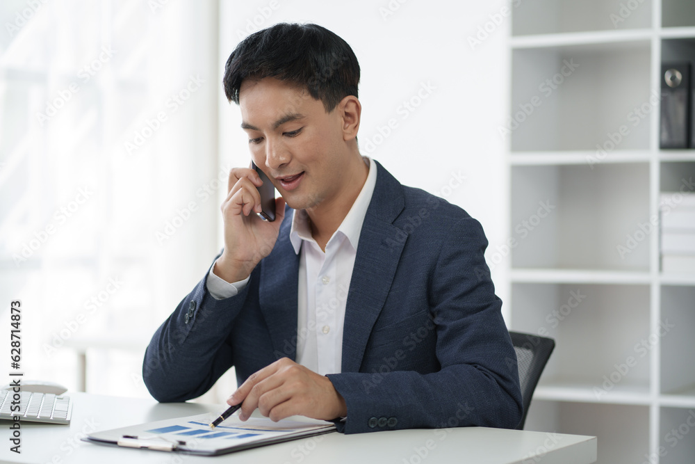 Young Asian businessman having a phone call with his client, discussing the details. Young Asian businessman having a phone call with his client, discussing the details.