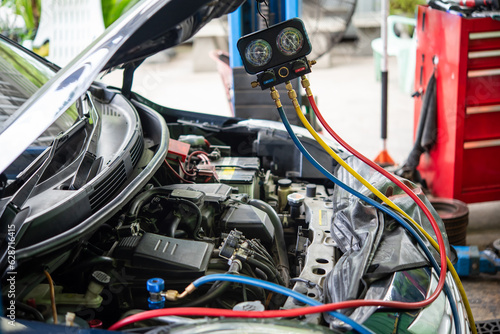 Car mechanic or serviceman refilling air condition and checking a air compressor for fix and repair problem at car garage or repair shop © pongmoji