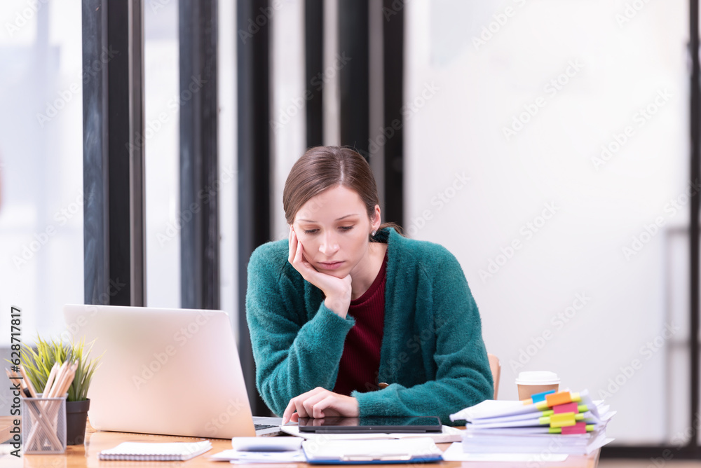 Businesswomen are stressed with work in front of a laptop and paper documents in the office. Businesswomen are stressed with work in front of a laptop and paper documents in the office.