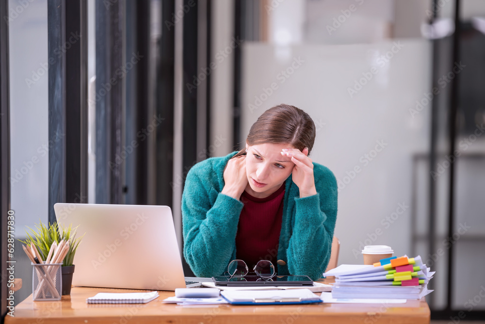Businesswomen are stressed with work in front of a laptop and paper documents in the office. Businesswomen are stressed with work in front of a laptop and paper documents in the office.