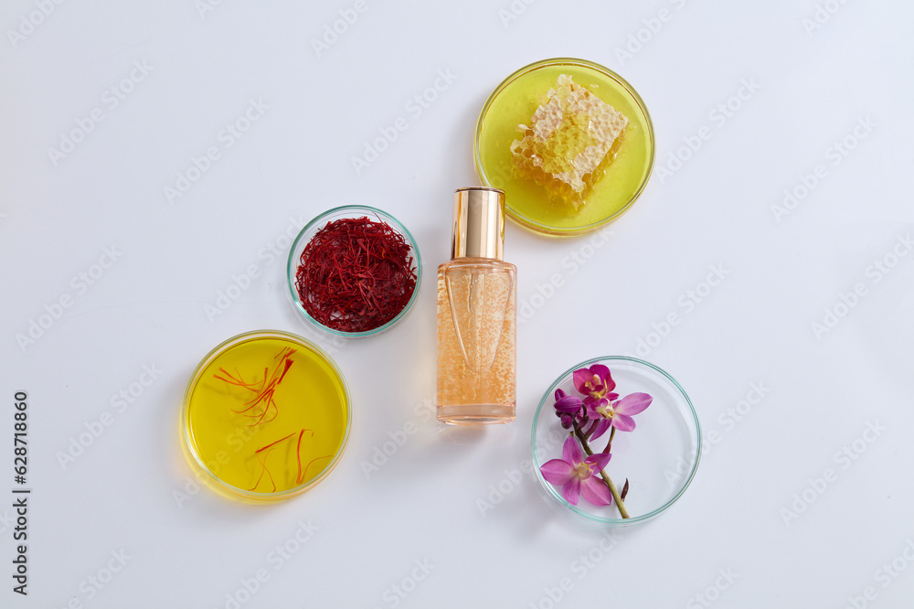 Serum bottle placed in the middle of several petri dishes of purple flowers, honeycomb and red saffron. Saffron was used in ancient times as a perfume Serum bottle placed in the middle of several petri dishes of purple flowers, honeycomb and red saffron. Saffron was used in ancient times as a perfume