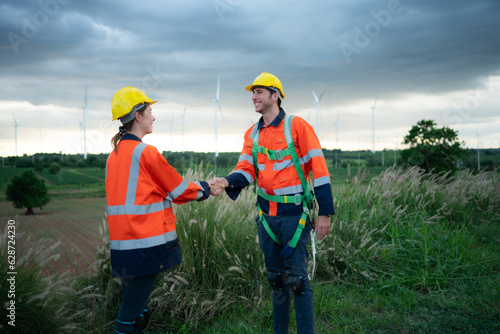Two engineers shaking hands on the background of wind turbines in the field