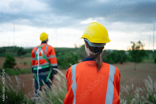 Young female engineer working in a wind turbine field and young man engineer wear a safety vest raise both hands to relax after finishing the wind turbine inspection mission