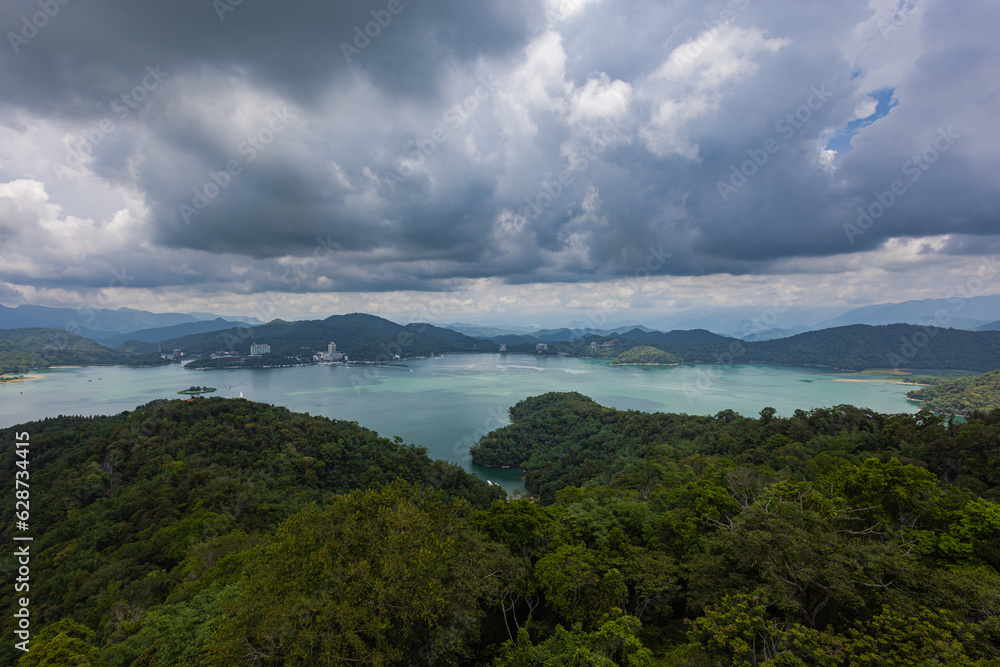 From Ci'en Pagoda, mesmerizing vista unfolds, panoramic view of Sun Moon Lake Taiwan, with surrounding mountain landscape. The tranquil lake mirrors the sky, while lush green peaks embrace its shores