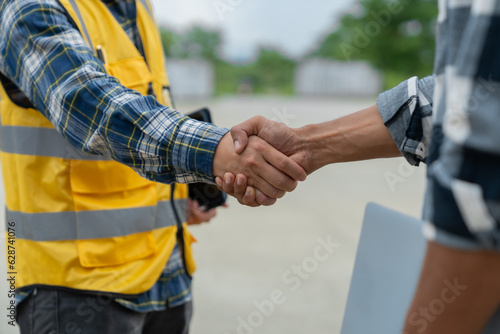 Asian engineer and architect shaking hands at construction site in the outdoor village project Teamwork and a successful housing project.