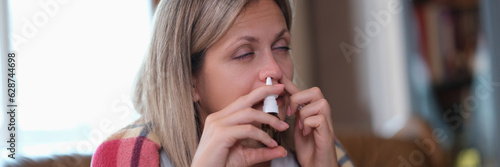 Woman with cold holds a nasal spray in her hand while sitting on couch at home.