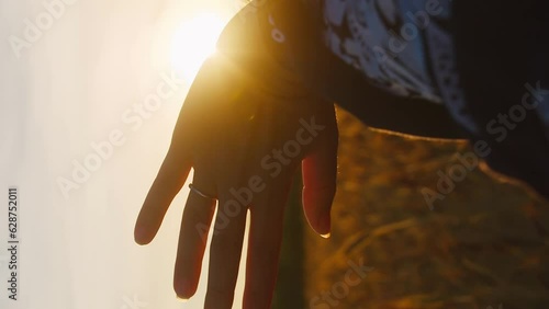 Vertical shot portrait of the girl looks at the sunset sun and plays with the rays of the sun that slip through her fingers  in evening rays of sunrise 
