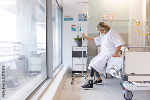 Senior caucasian female patient with prosthetic leg sitting on bed at hospital, copy space