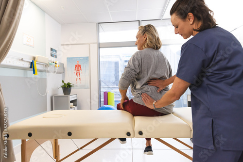 Caucasian female physiotherapist and senior woman massaging back at hospital
