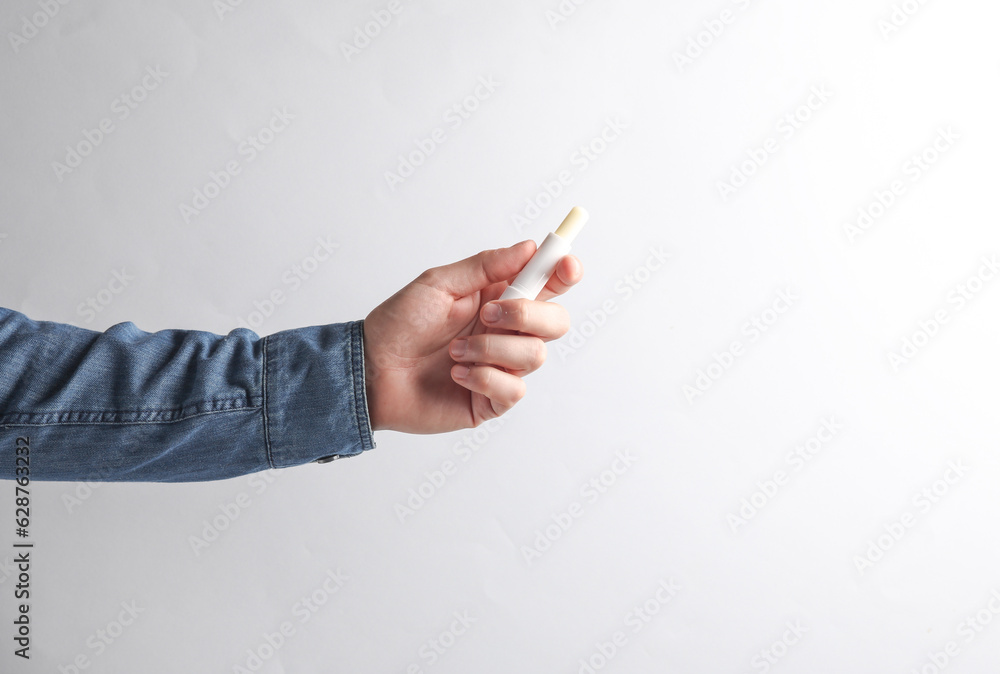 Man's hand in denim shirt holding lips balm on gray background. Man's hand in denim shirt holding lips balm on gray background.