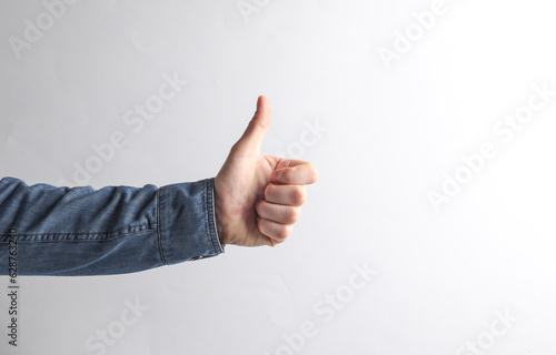 Man's hand in a denim shirt shows a thumbs up on a gray background photo