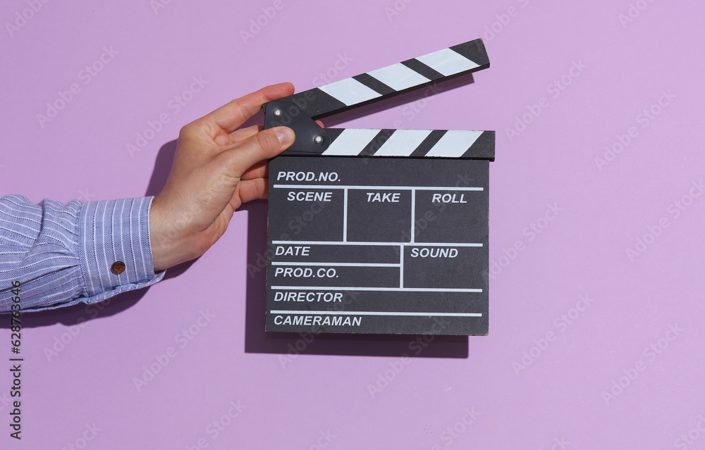 Man's hand in shirt holding clapperboard on purple pastel background with shadow.