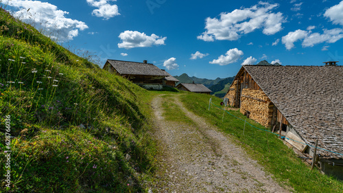 Holzhaus auf der Alpe Steris im Grosswalsertal, Vorarlberg, mit steilen Bergwiesen, Wald und Bergen im Hintergrund, Dorf am Abhang auf einer Hochebene in Österreich
