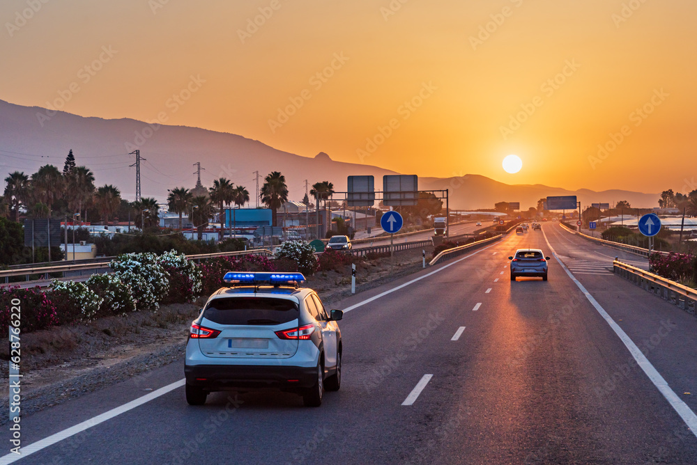 Traffic police car driving on a highway with the early morning sun rising over the mountains on the horizon. Traffic police car driving on a highway with the early morning sun rising over the mountains on the horizon.
