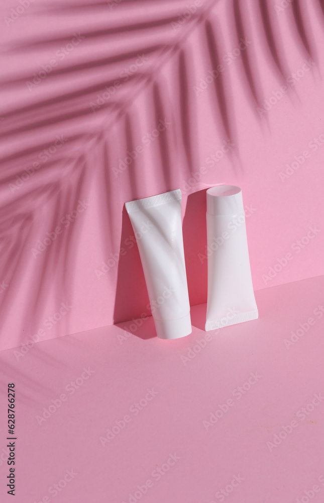 White cream tube on pink background with palm leaf shadow. Creative beauty layout. Mockup, template for design White cream tube on pink background with palm leaf shadow. Creative beauty layout. Mockup, template for design