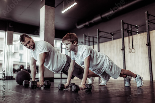 Healthy family concept. Father trainer and teenager son push ups with dumbbells in gym. Fitness, sports, active lifestyle