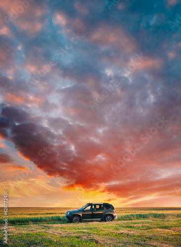 AWD 4WD SUV green car in summer meadow landscape in summer field countryside landscape. Sunset sky background.