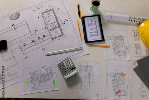 Overhead view of desk with architectural blueprints, tablet, coffee and hardhat