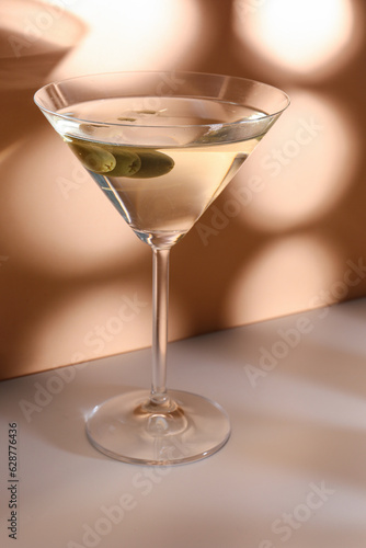 Glass of martini with olives on color background