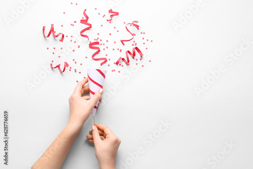Female hands with party popper and confetti on light background